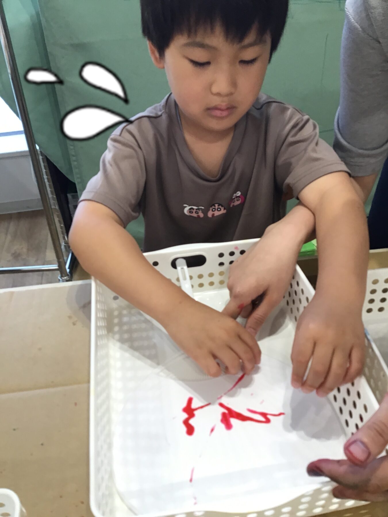 Young boy concentrating on drawing with a red marker inside a white perforated basket on a table.