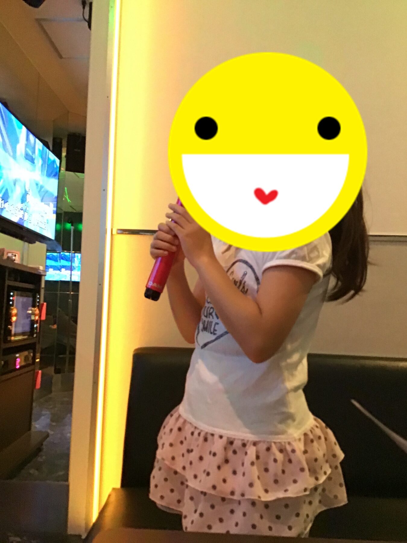 Girl on stage singing into a pink microphone, wearing a white shirt and pink polka-dot skirt.
