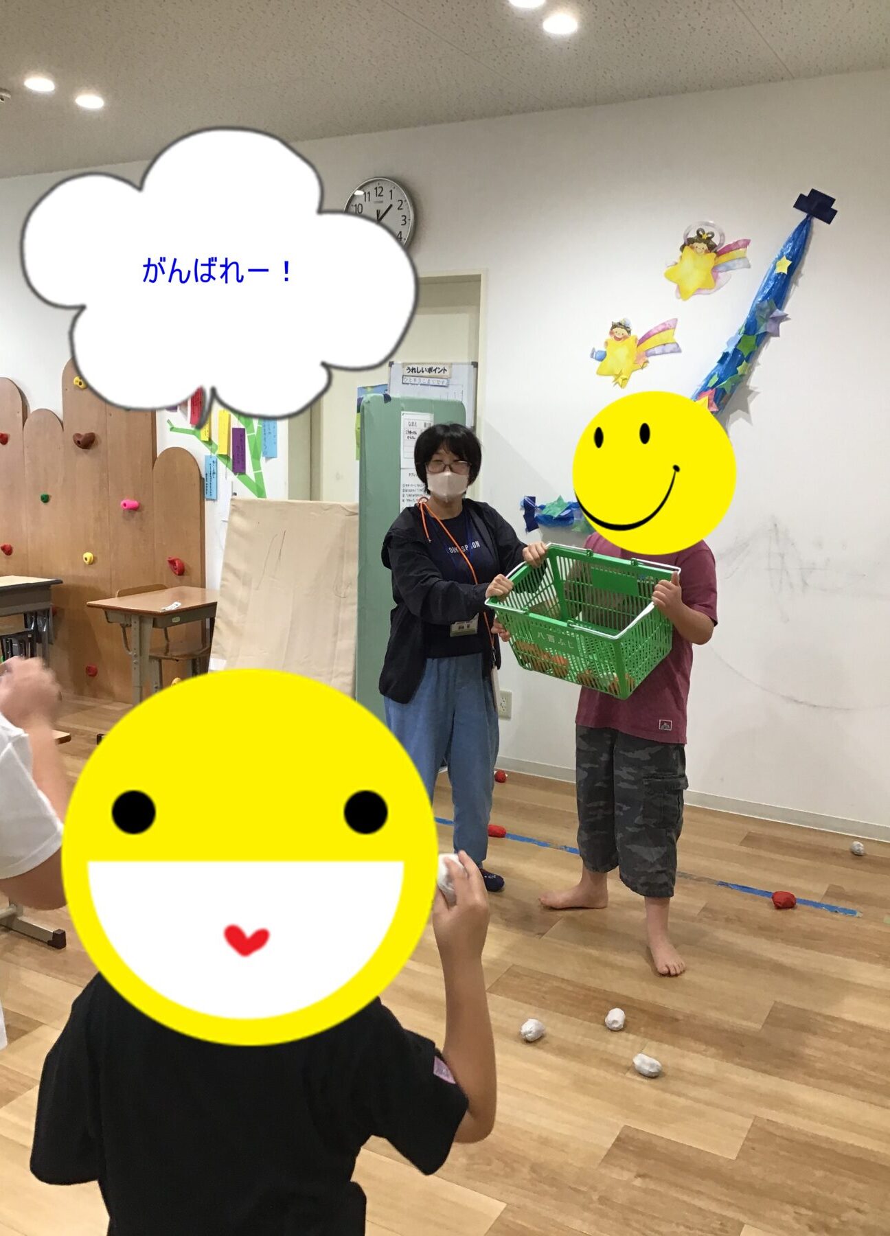 Teacher in a mask hands a green basket to a student in a decorated classroom; clock on the wall and smilesy overlays are visible in the scene.