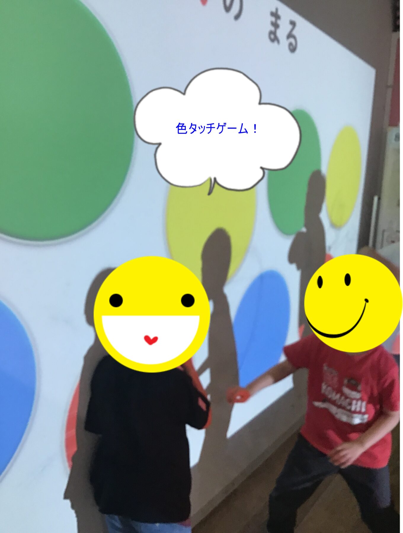 Two kids with smiley-face stickers on their faces stand in front of a colorful mural, raising hands; speech bubble shows Japanese text: 色々ッチゲーム!
