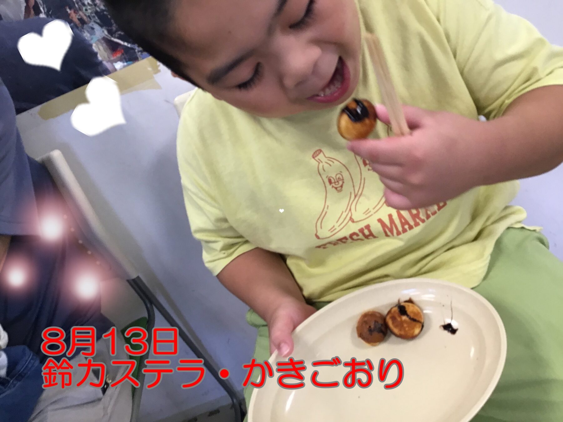 Child in a pale yellow shirt eats small round pastries from a plate, using chopsticks to pick one up.