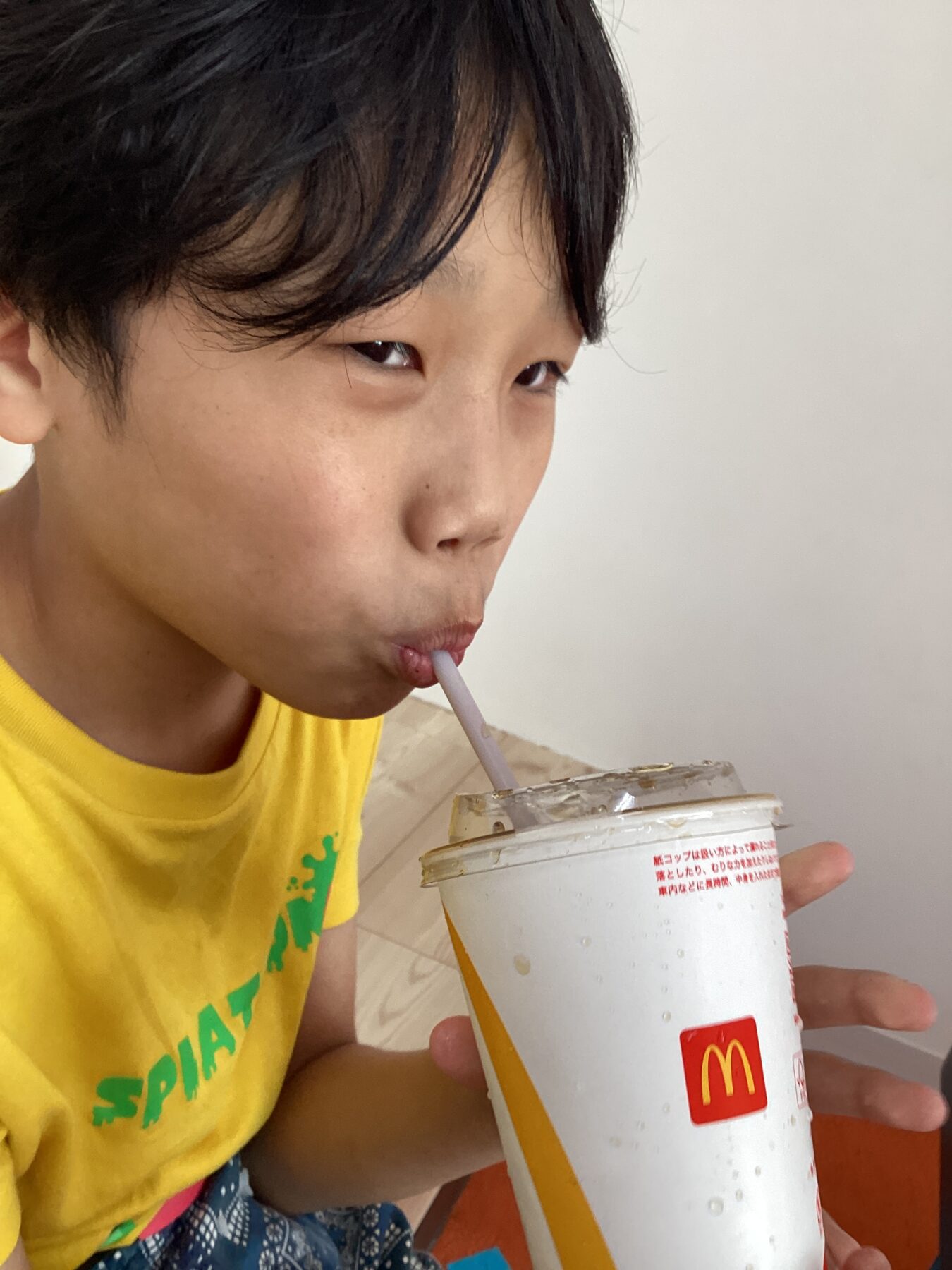 Child wearing a yellow shirt sips a drink with a straw from a McDonald's cup.