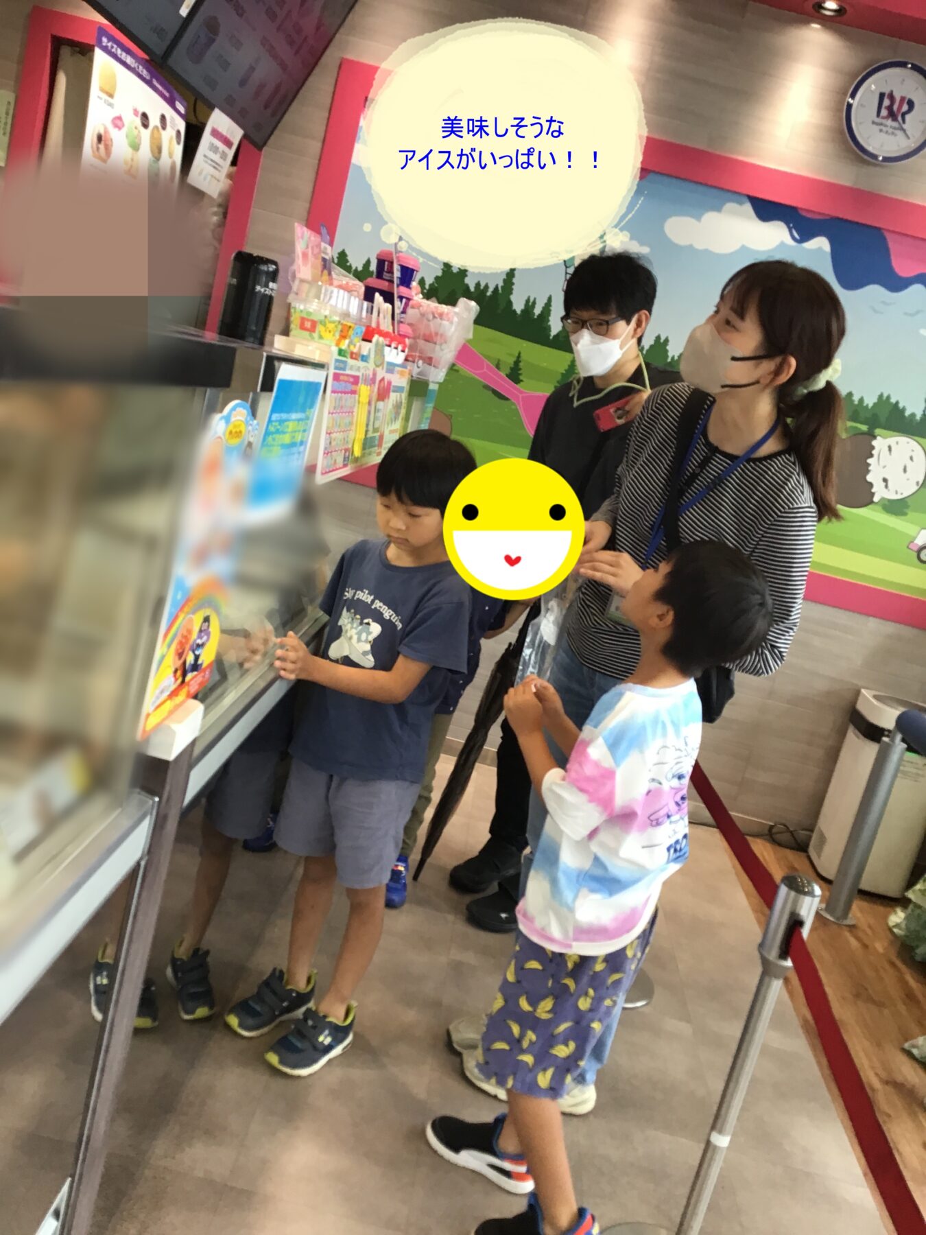 Children and two adults wearing masks stand at a colorful ice-cream counter, one child pointing at treats; a speech bubble in Japanese reads '美味しそうなアイスがいっぱい！！'