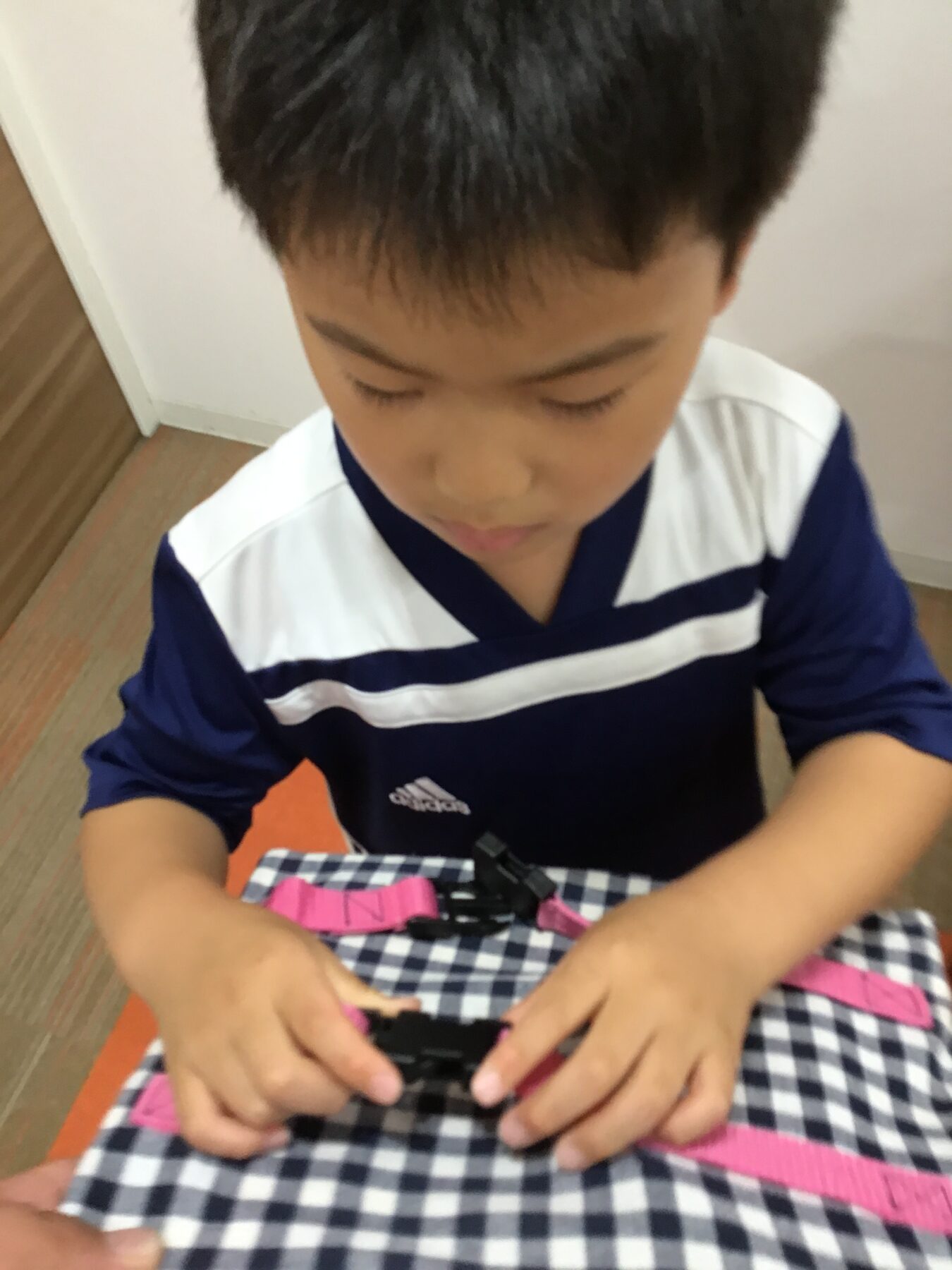 Boy wearing a navy blue and white striped shirt looks down at a puzzle on a checkered table.