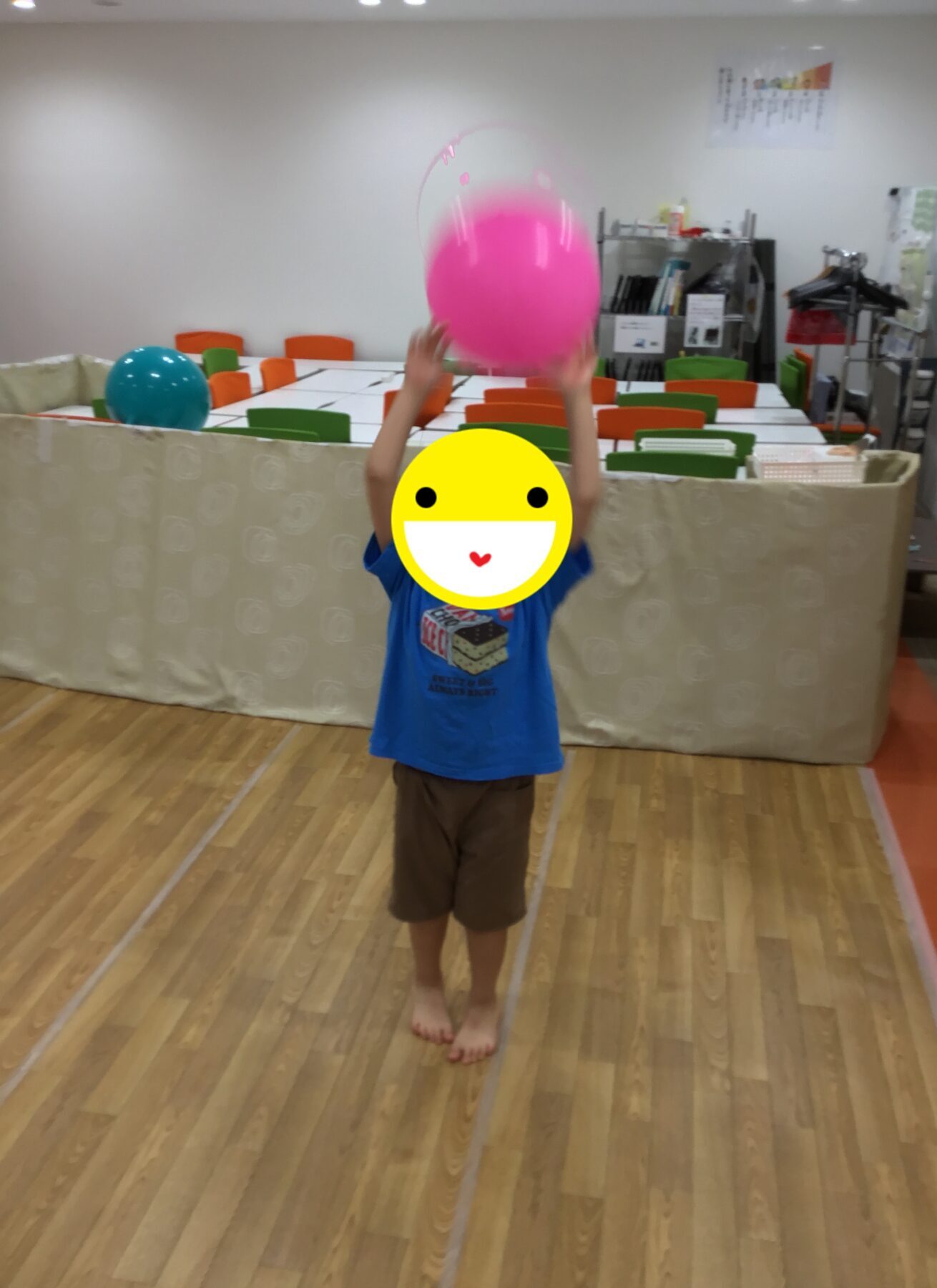 Child standing in a playroom, tossing a large pink balloon above their head.