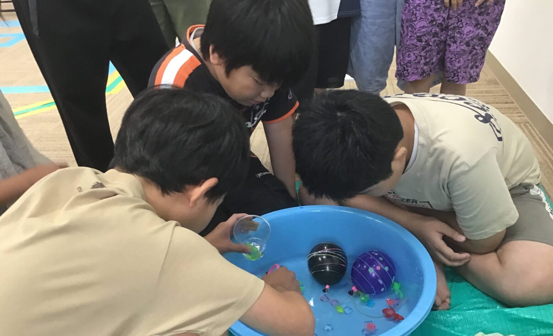 Children kneeling around a blue tub, fishing for small floating toys in water during a group activity.