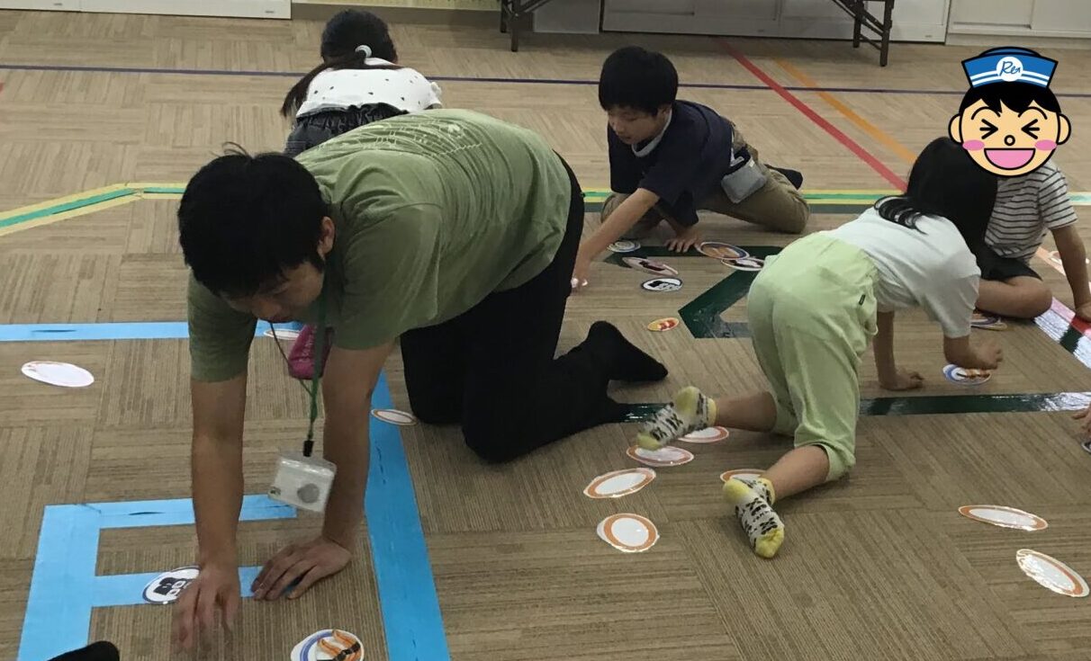 Group of people kneeling on a gym floor, placing circular game cards along taped lines as part of a classroom activity.