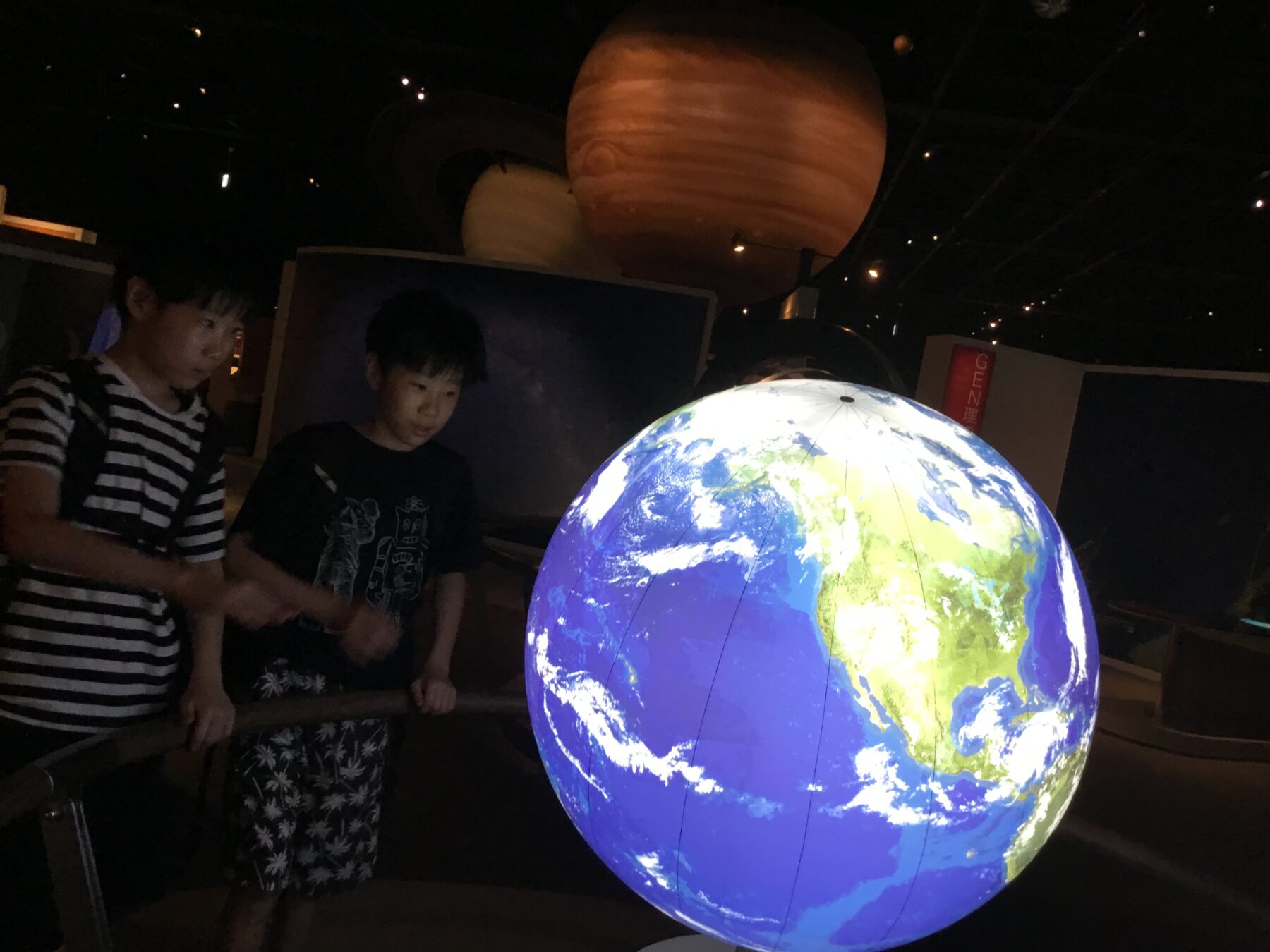 Two children gaze at a glowing globe of Earth in a dark science museum.