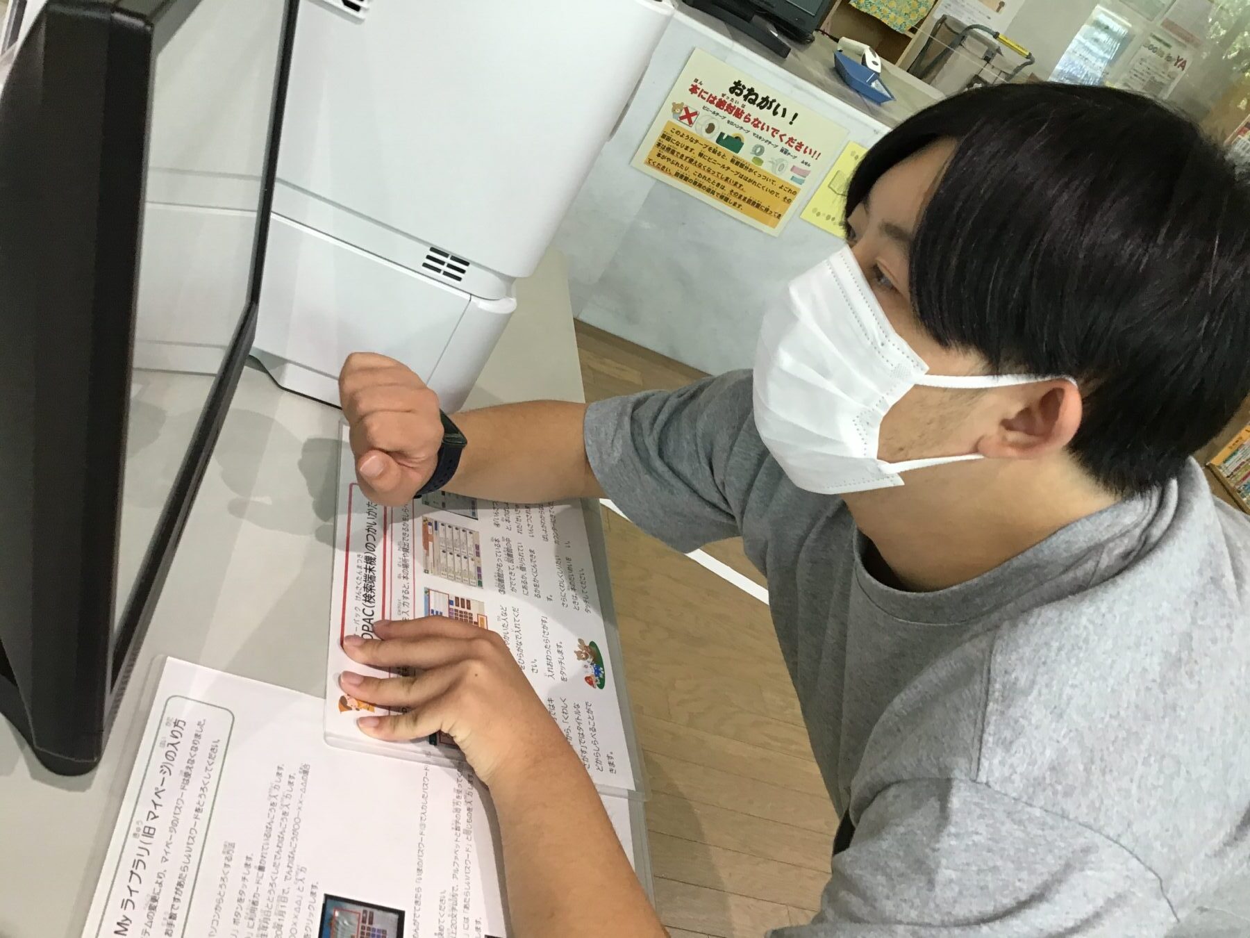 Person wearing a white mask leaning over a desk, signing a form near a printer in a shop or office.