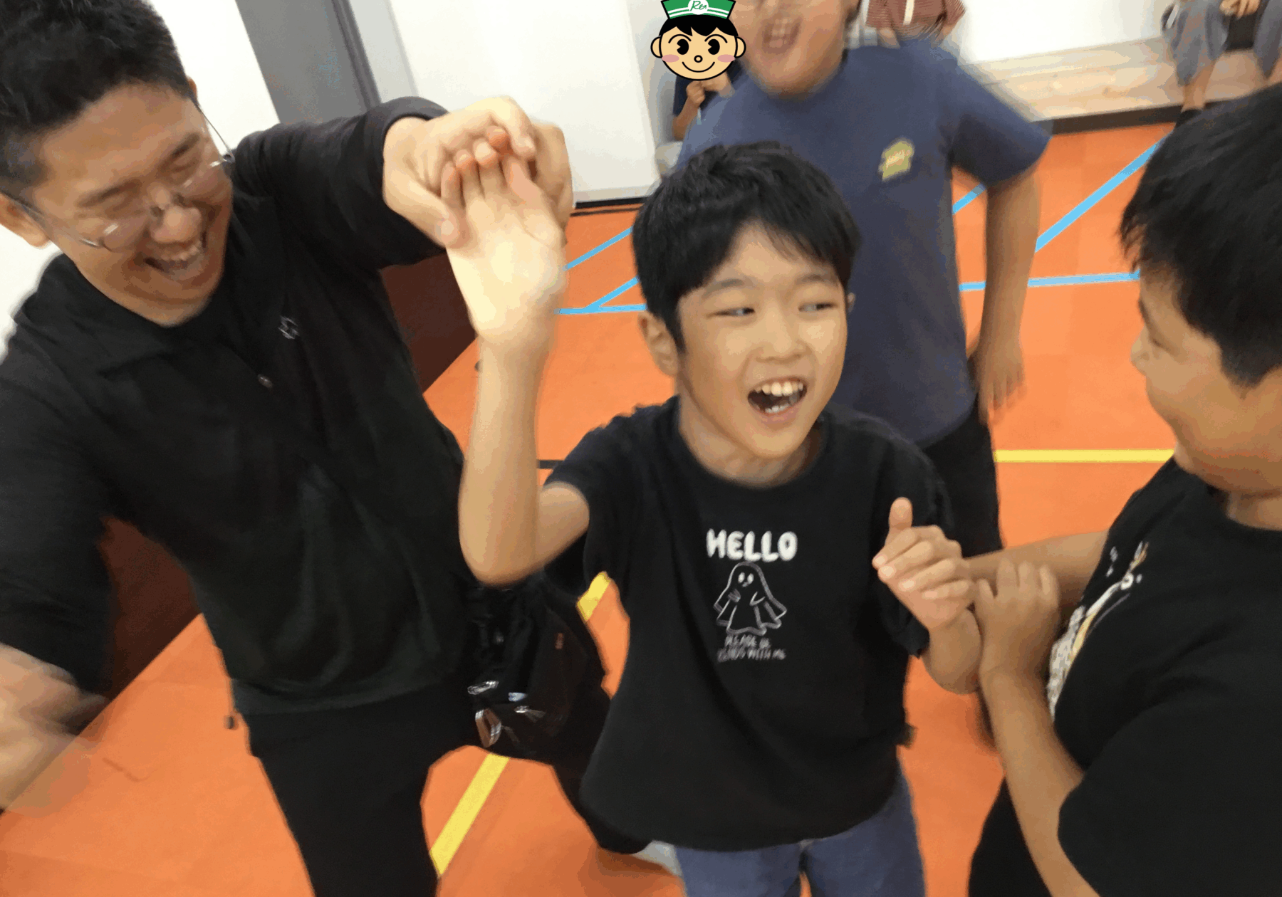 A smiling boy in a black shirt high-fives teammates in a gym with an orange floor and blue lines behind him