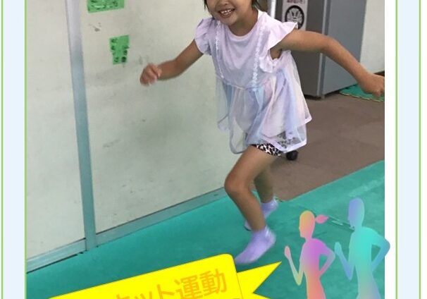 Young girl in a white dress runs on a green gym floor indoors, smiling, with a yellow ribbon displaying 'サーキット運動' (circuit exercise) and decorative border elements like clouds and dancing silhouettes.