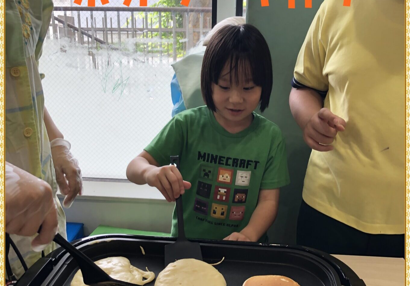 Kids cooking fluffy pancakes on a griddle, with orange Japanese text overlay reading ふわふわホットケーキ作り.
