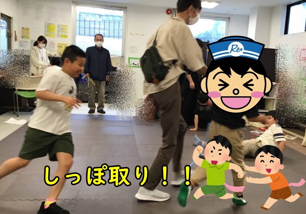 A child runs across a padded play area while adults and other kids watch; cartoon characters and Japanese text cover part of the scene.