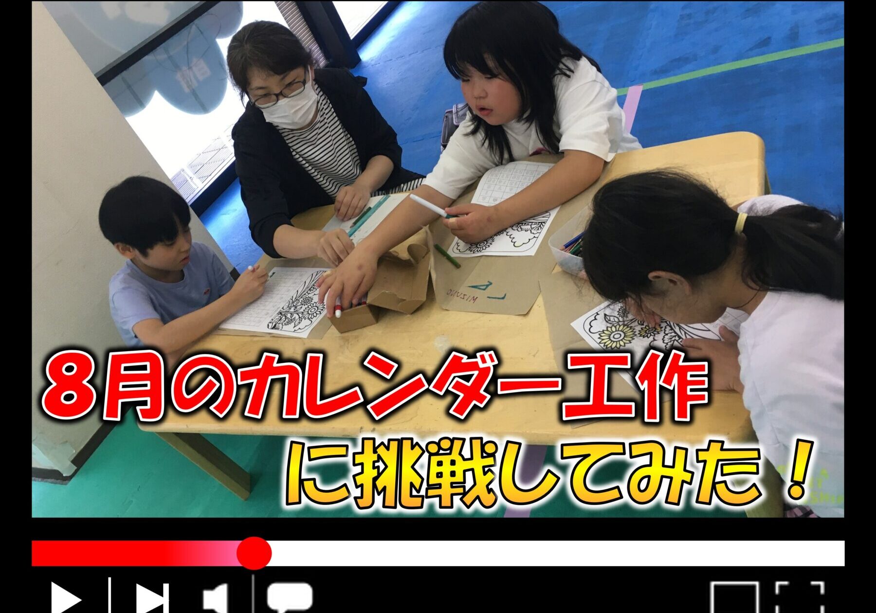 Children and a teacher coloring calendars at a table with markers and worksheets in a classroom.