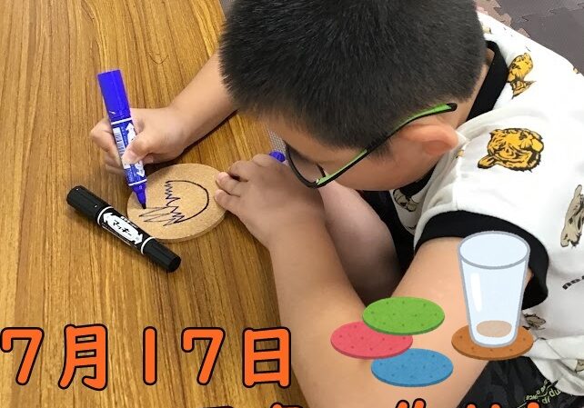A young boy with glasses colors a round cork coaster with a blue marker on a wooden table.