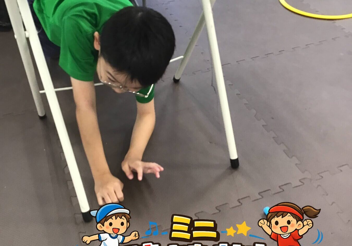 Child in a green shirt crawls under a table as part of an indoor obstacle course on foam mat with yellow circular markers.