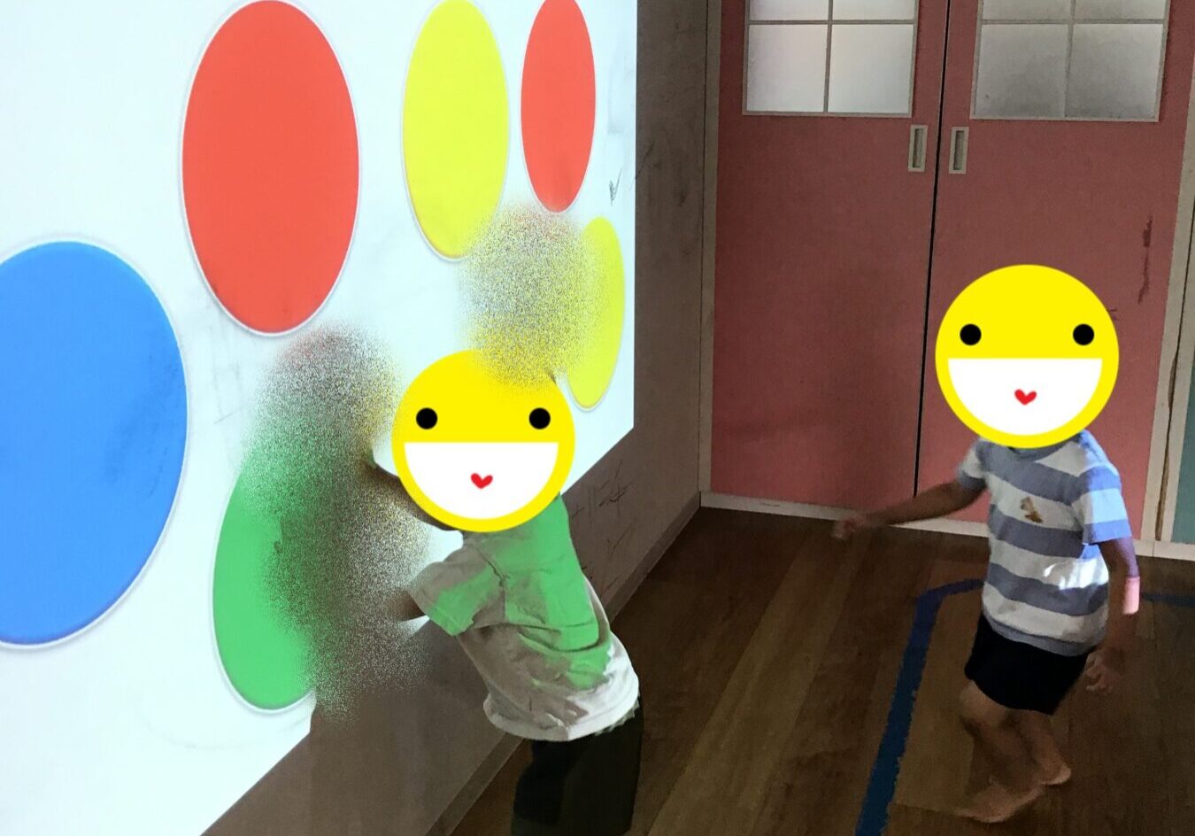Children interact with a wall display of large colored circles (red, yellow, blue, green) as part of a color activity in a classroom.