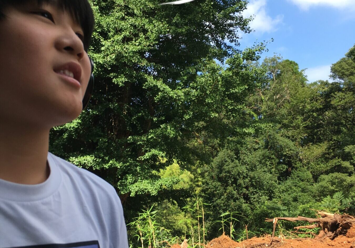 Person outdoors with trees behind, wearing a white shirt and headphones, speech bubble reading '熊野那智神社に行ってきました！' (I went to Kumano Nachi Shrine!).