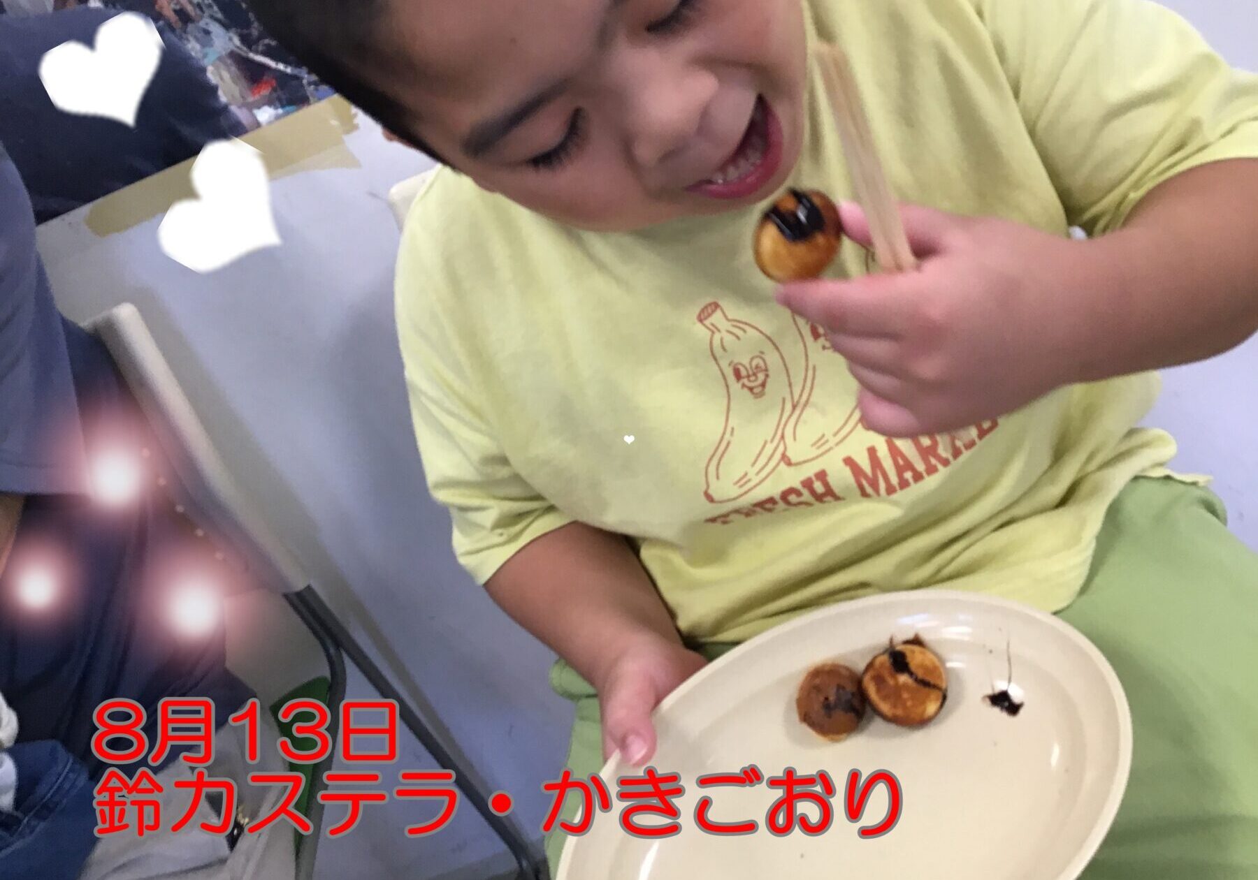 Child in a pale yellow shirt eats small round pastries from a plate, using chopsticks to pick one up.