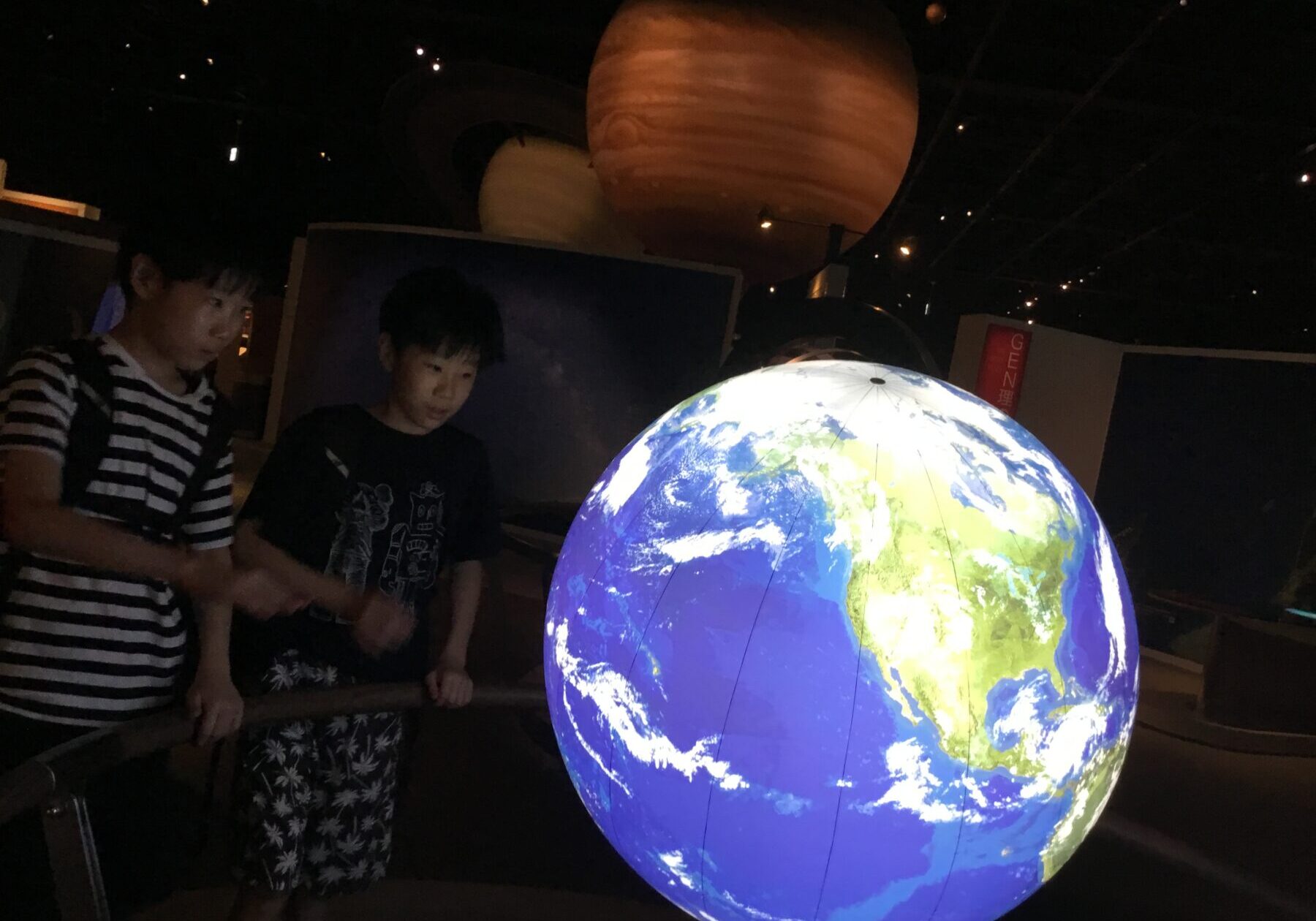 Two children gaze at a glowing globe of Earth in a dark science museum.
